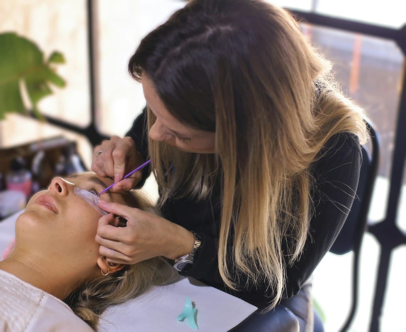 Une technicienne en pose de cils travaille au domicile d’une cliente