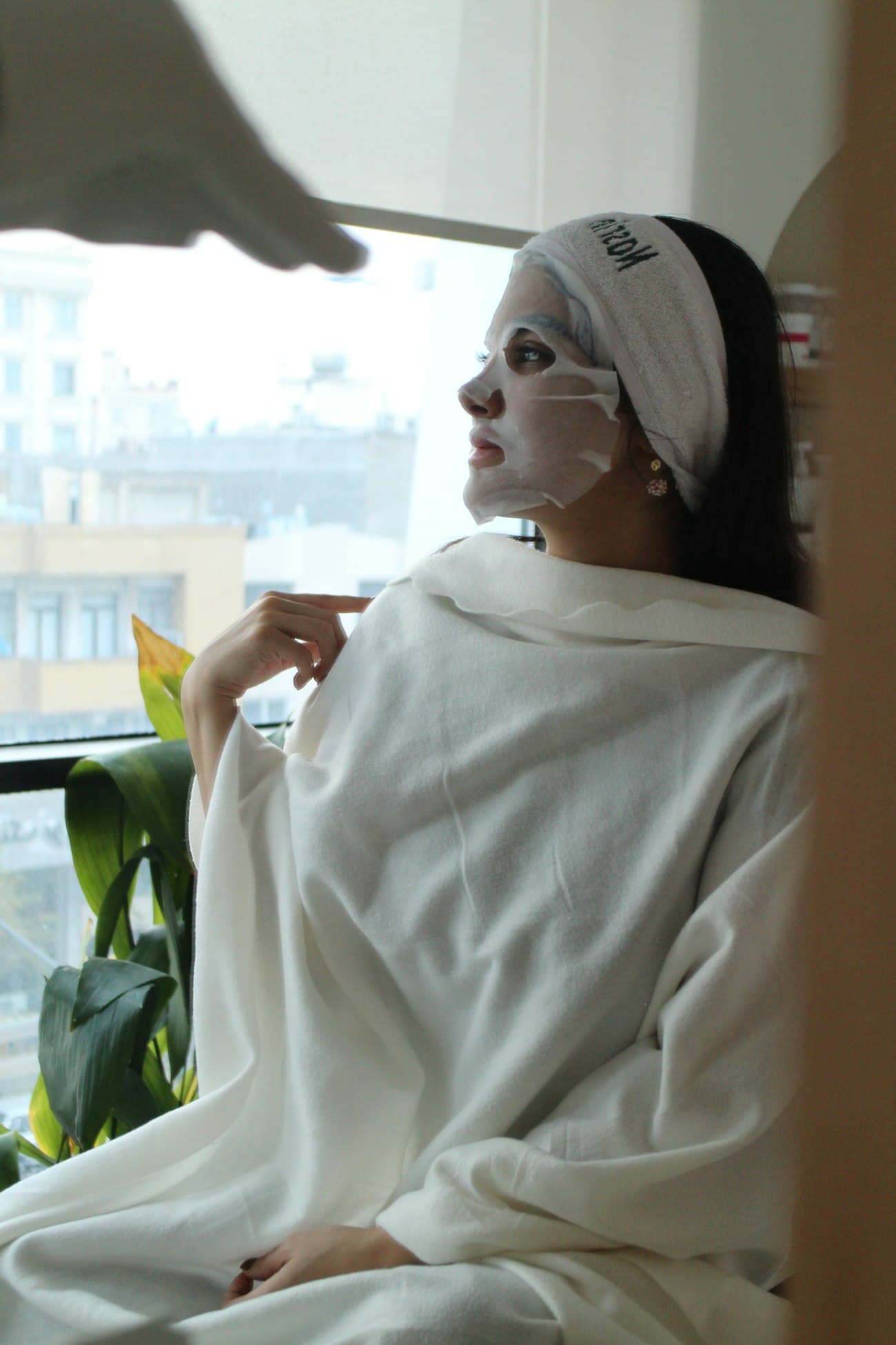 Une cliente en peignoir profite d’un soin du visage à la maison, près d’une fenêtre